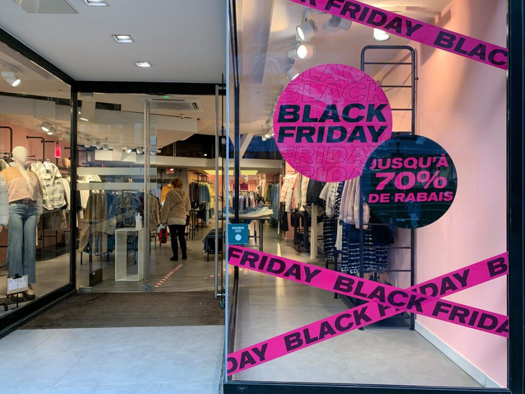 Vitrine Black Friday : bandes adhésives roses et pastilles promotionnelles posées sur la vitrine d'une boutique de vêtements